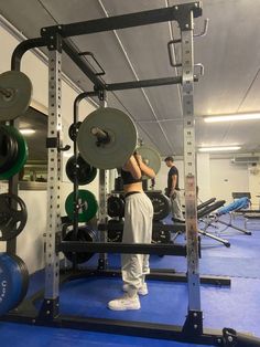 a woman standing in front of a gym equipment rack with two men working out behind her