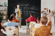 a man standing in front of a blackboard giving a class to children sitting at desks