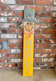 a yellow sign with a scarecrow on it next to a brick wall and potted plant