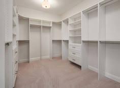 an empty walk in closet with white shelves and drawers