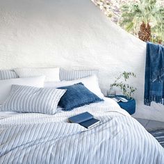 a bed with blue and white striped linens on it, next to a window