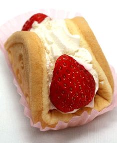 a small pastry with whipped cream and strawberries on it's side, sitting on a pink paper wrapper