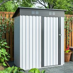 a white and gray shed sitting next to a wooden fence in the middle of a yard