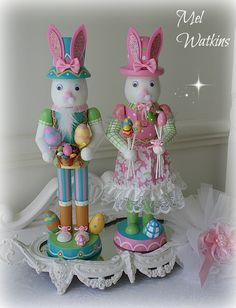 two bunny figurines sitting on top of a table next to an easter decoration