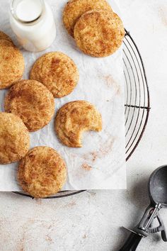 some biscuits are on a wire rack next to a cup of milk and a spoon