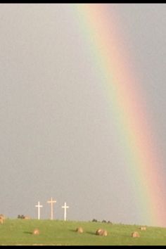 a rainbow in the sky over a green field with hay bales and crosses behind it