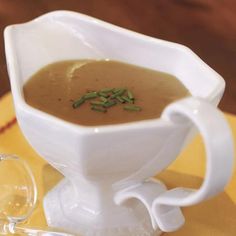 a white gravy dish on a yellow place mat with a spoon and glass goblet