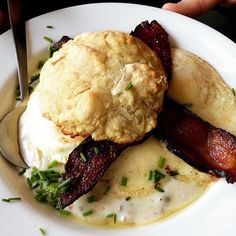 a white plate topped with bacon and biscuits on top of mashed potatoes