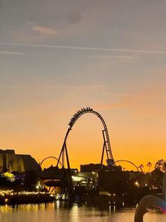 an amusement park at sunset with roller coasters in the distance and lights reflecting on the water