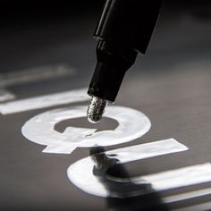 a close up of a metal object with a pen in it's mouth and some letters on the surface