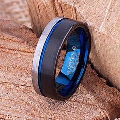 a black and blue wedding ring sitting on top of a piece of wood