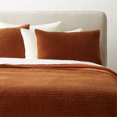 a bed with two pillows on top of it and an orange blanket over the headboard