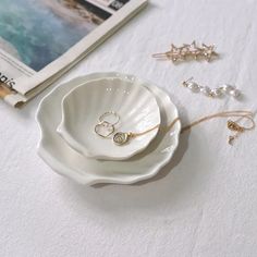 two rings are sitting in a shell shaped bowl next to other jewelry on a table