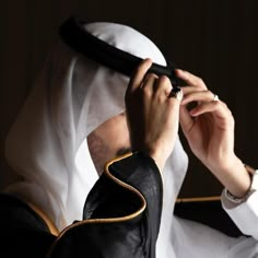 a person in a white headdress holding something up to their face with both hands