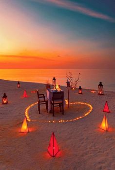 a table set up on the beach with lanterns and candles in the shape of a heart