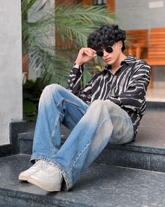 a young man sitting on the steps wearing jeans and a zebra print shirt with his hands in his eyes