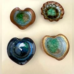 four heart shaped bowls sitting next to each other on a white counter top, one with green and blue glaze in the middle