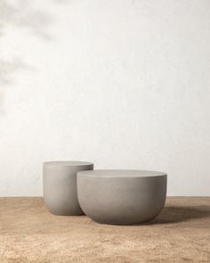 two concrete bowls sitting next to each other on a wooden table in front of a white wall