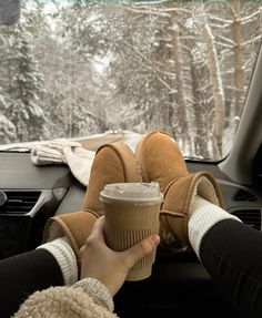 someone is holding a coffee cup in their hand while driving through the snow covered forest