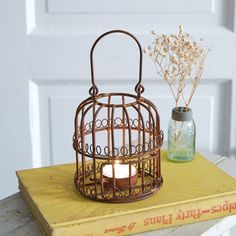 a small birdcage with a candle inside sits on top of a yellow book