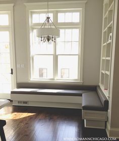 a living room with wood floors and a window seat in the corner next to a book shelf