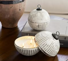 two white ceramic balls sitting on top of a table next to a book and candle