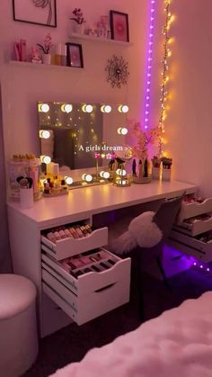 a white desk topped with lots of drawers under a purple light filled mirror next to a bed