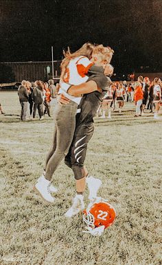 two girls hugging each other in the middle of a field with football players and fans behind them