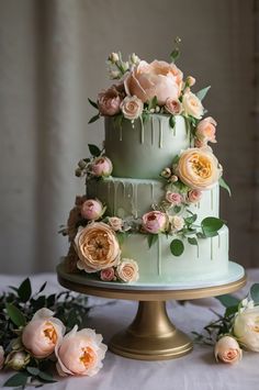 a three tiered cake with flowers on top and greenery around the edges, sitting on a gold pedestal