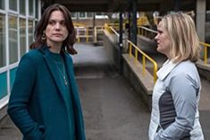 two women are standing in front of a building and one is looking at the other