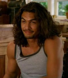 a man with long hair sitting in a kitchen