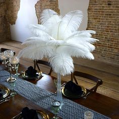 the table is set with black and white place settings, silverware, and an ostrich feather centerpiece