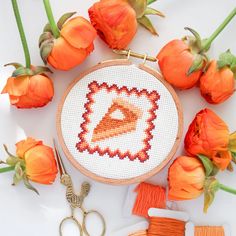 a cross stitch project with orange flowers and scissors