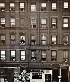 an old black and white photo of people looking out the windows of a tall building