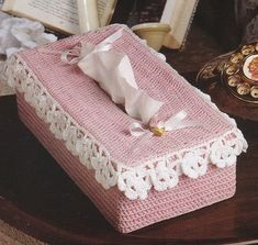 a pink crocheted box sitting on top of a table next to an open book