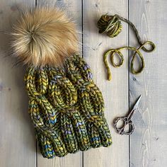 a knitted hat with a pom - pom next to scissors and yarn