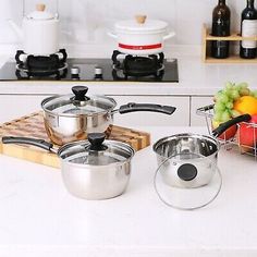 pots and pans are sitting on the counter in front of some wine bottles, oranges, and other cooking utensils