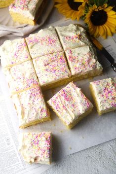 there are many pieces of cake on the table next to some flowers and a knife