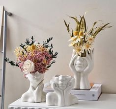 two white vases with flowers in them sitting on a shelf next to each other