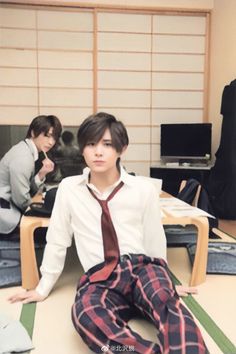 two young men sitting on the floor in front of desks with computers and papers