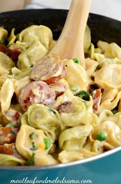 a skillet filled with pasta and vegetables on top of a table next to a wooden spoon