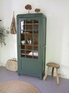 a green cabinet sitting in the corner of a room next to a chair and table