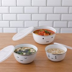 three bowls with different types of food in them on a wooden table next to a white brick wall