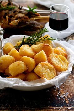 a white bowl filled with fried food on top of a wooden table next to a glass of wine