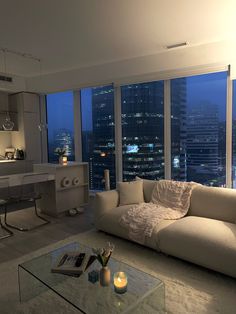 a living room filled with furniture and large windows overlooking the city lights at night time