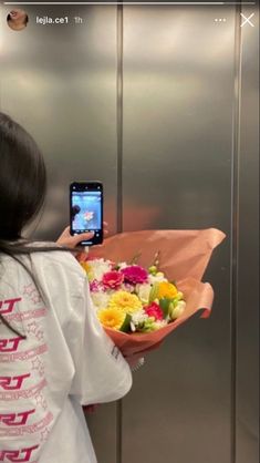 a woman taking a selfie with her cell phone while holding a bouquet of flowers