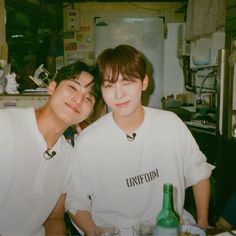 two young men sitting next to each other in front of a table with food and drinks on it