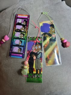 three cartoon bookmarks are laying on a bed with beads and necklaces around them