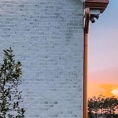 an orange fire hydrant in front of a white brick building with the sun setting behind it