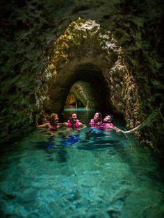 three people are swimming in the water inside an underground cave that is filled with clear blue water